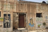 Image of a wall with murals drawn on and bullet holes left after the recent conflict.