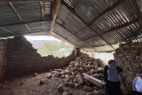 Mary's Meals member of staff stands next to a collapsed wall.