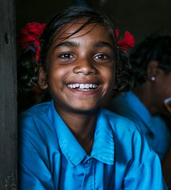 Image of a girl smiling into camera while classmates sit at their desks in the background.