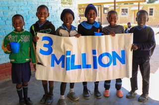 Children posing with a banner that reads "3 Million"